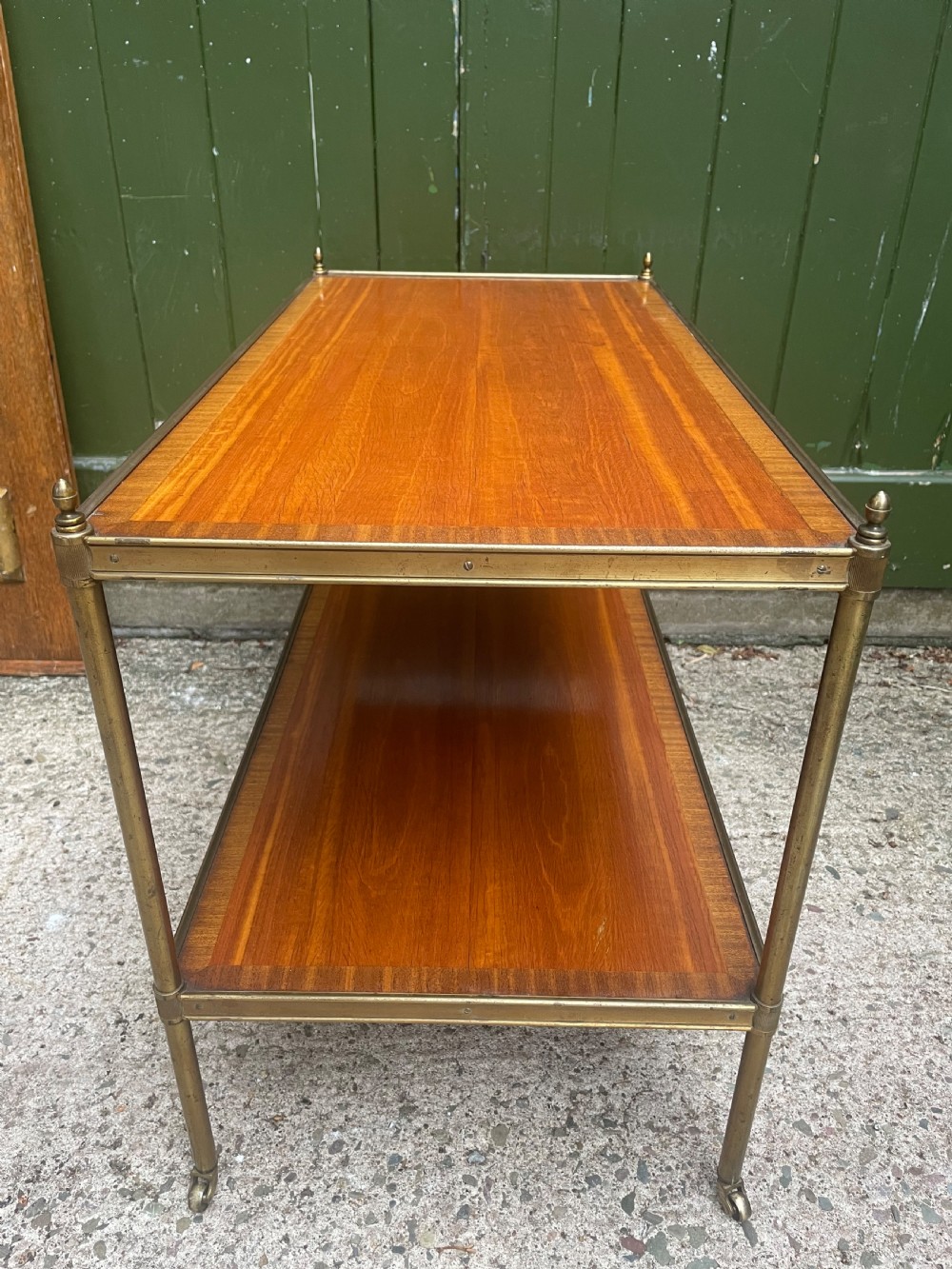 A low rectangular two-tier etagere table featuring satinwood shelves with decorative crossbanded inlay and a brass frame on castors. View VII