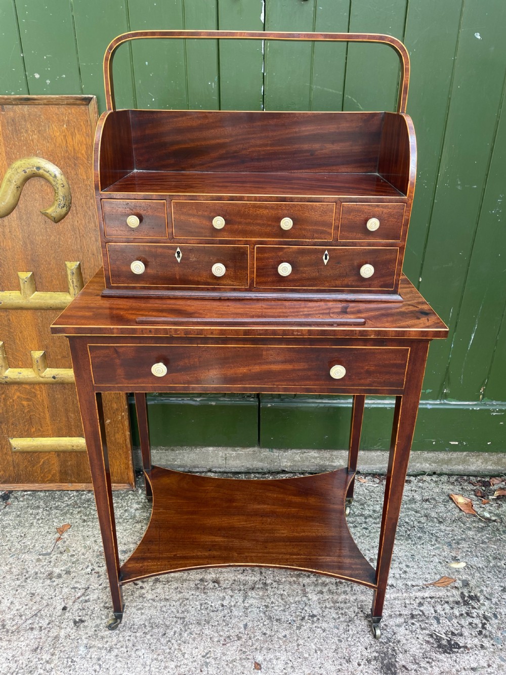 A late 18th-century George III Sheraton mahogany cheveret writing desk featuring a removable upper drawer section with an arched handle, line inlay, and tapered square legs on castors.