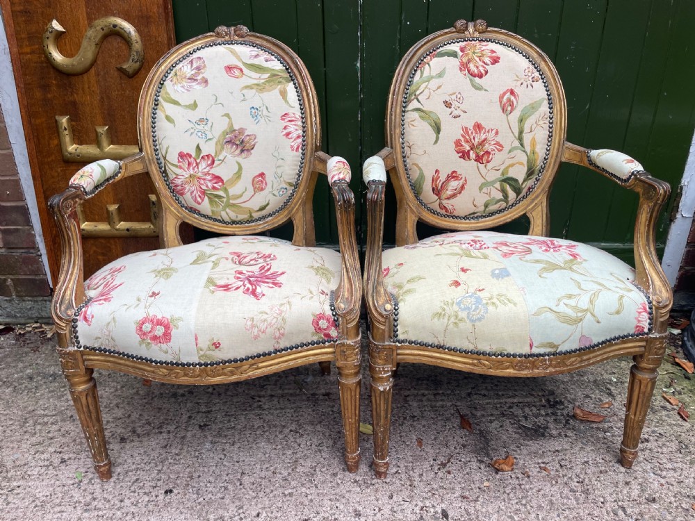 A pair of mid-19th-century French Louis XVI style giltwood salon armchairs with oval backs and floral upholstery.