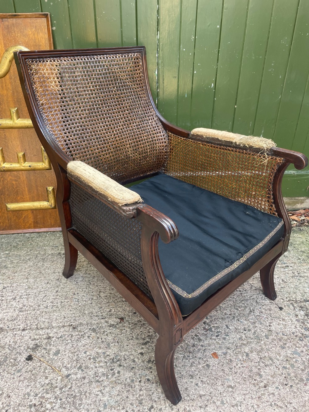 An early 19th-century Regency mahogany bergere armchair with woven cane back and sides, curved armrests, and a dark squab cushion.