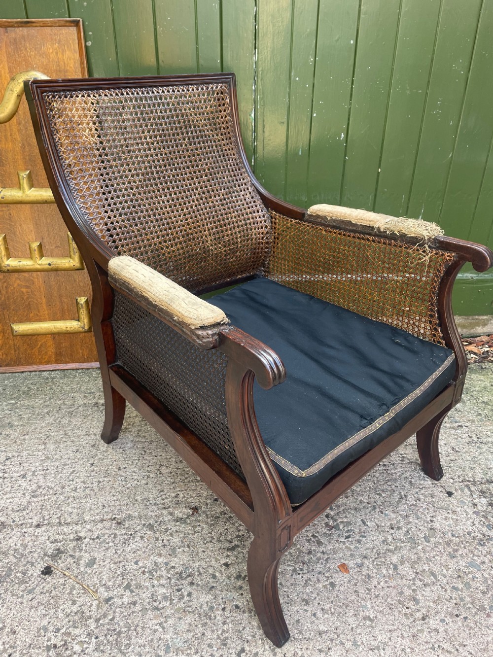 An early 19th-century Regency mahogany bergere armchair with woven cane back and sides, curved armrests, and a dark squab cushion. View II
