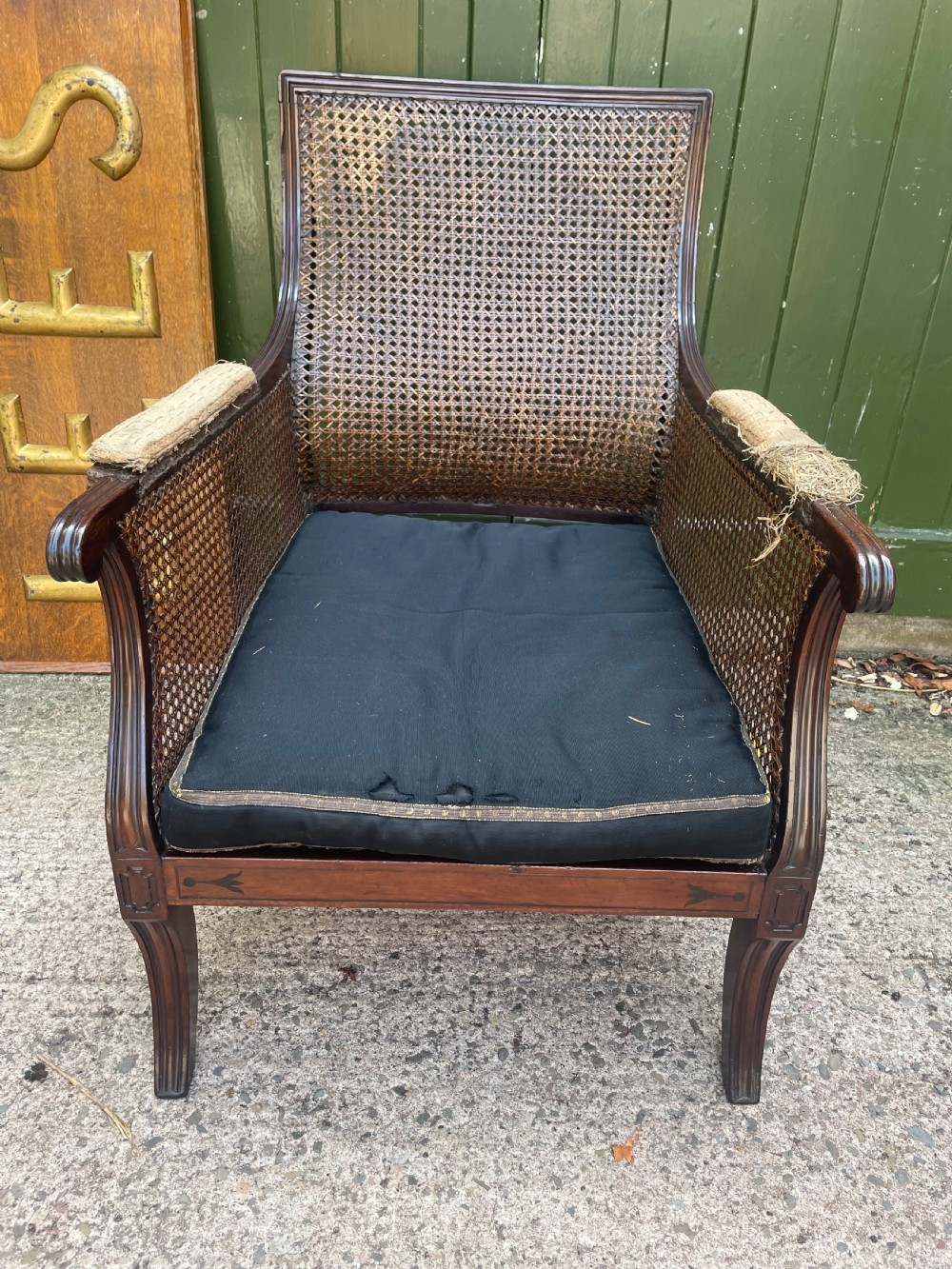An early 19th-century Regency mahogany bergere armchair with woven cane back and sides, curved armrests, and a dark squab cushion. View III