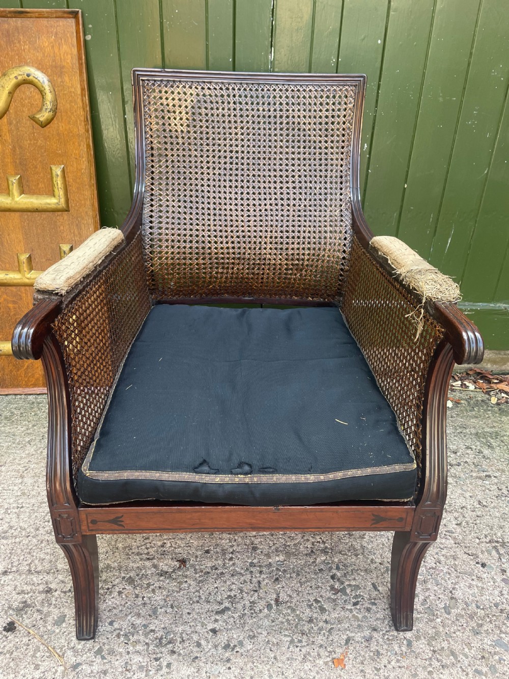 An early 19th-century Regency mahogany bergere armchair with woven cane back and sides, curved armrests, and a dark squab cushion. View V