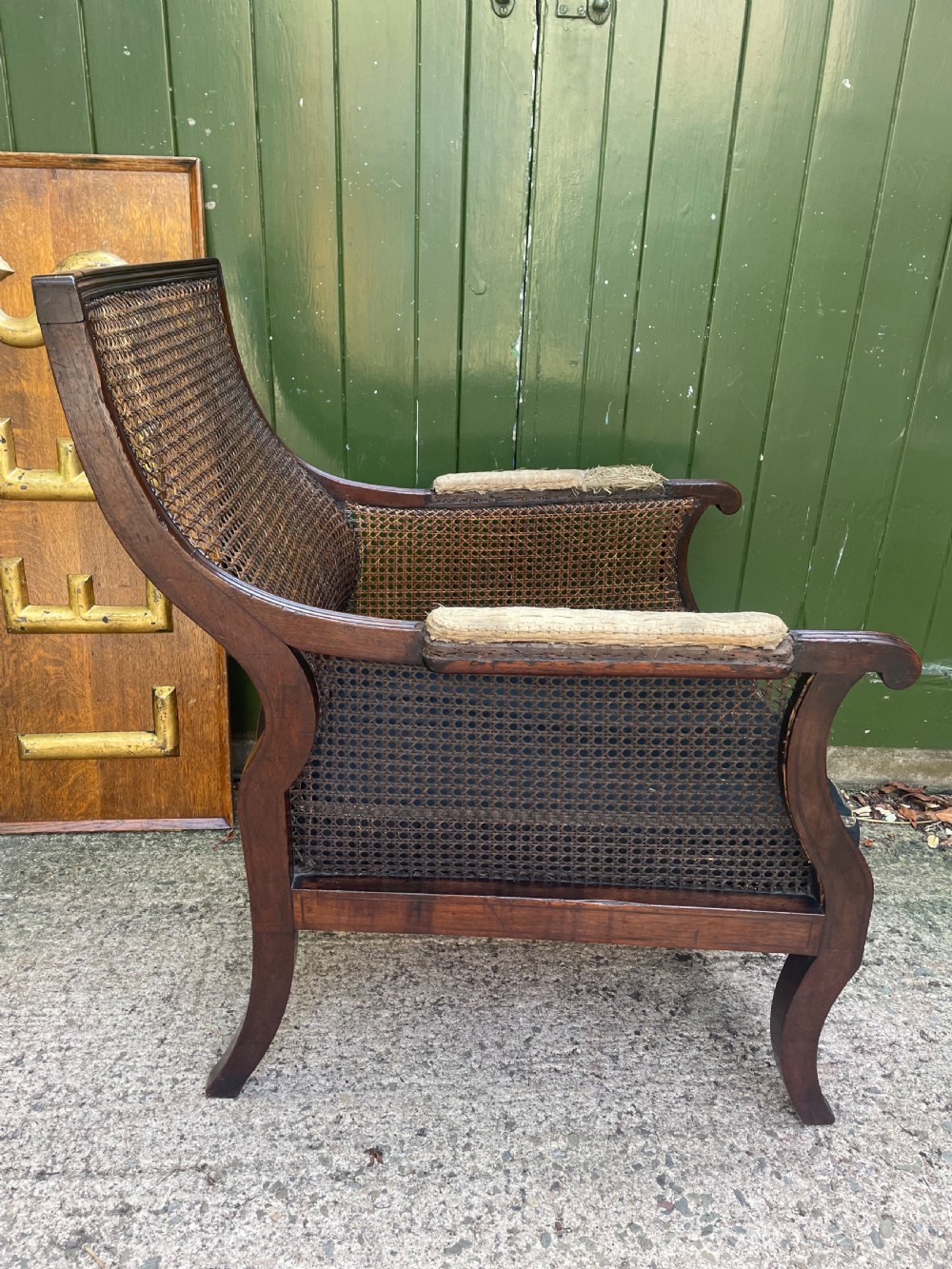 An early 19th-century Regency mahogany bergere armchair with woven cane back and sides, curved armrests, and a dark squab cushion. View IX