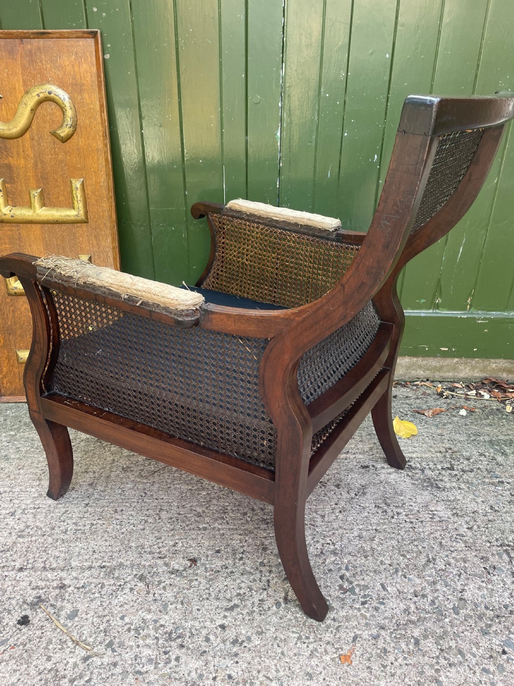 An early 19th-century Regency mahogany bergere armchair with woven cane back and sides, curved armrests, and a dark squab cushion. View X