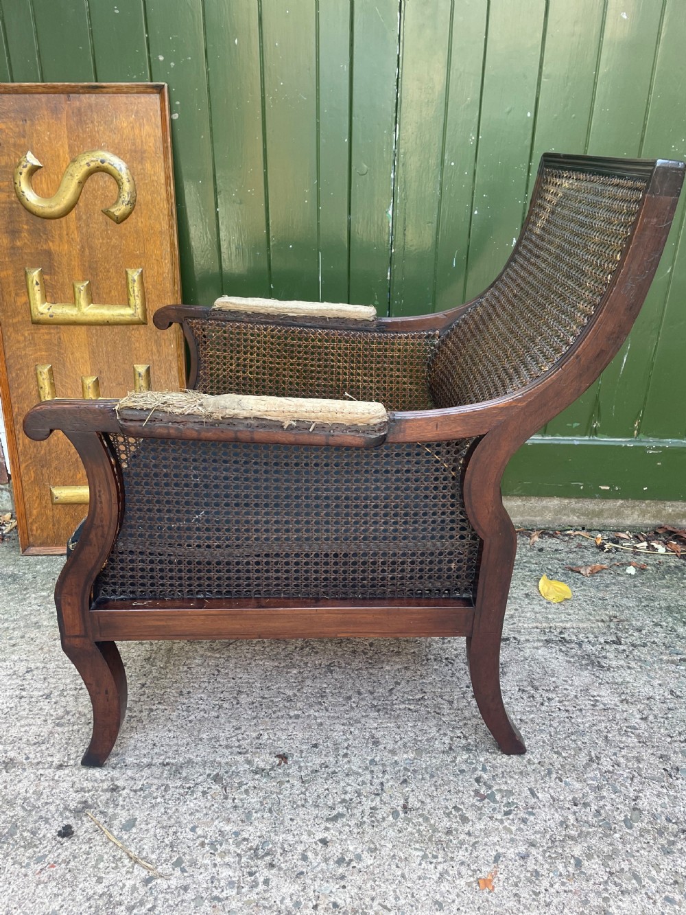 An early 19th-century Regency mahogany bergere armchair with woven cane back and sides, curved armrests, and a dark squab cushion. View XI