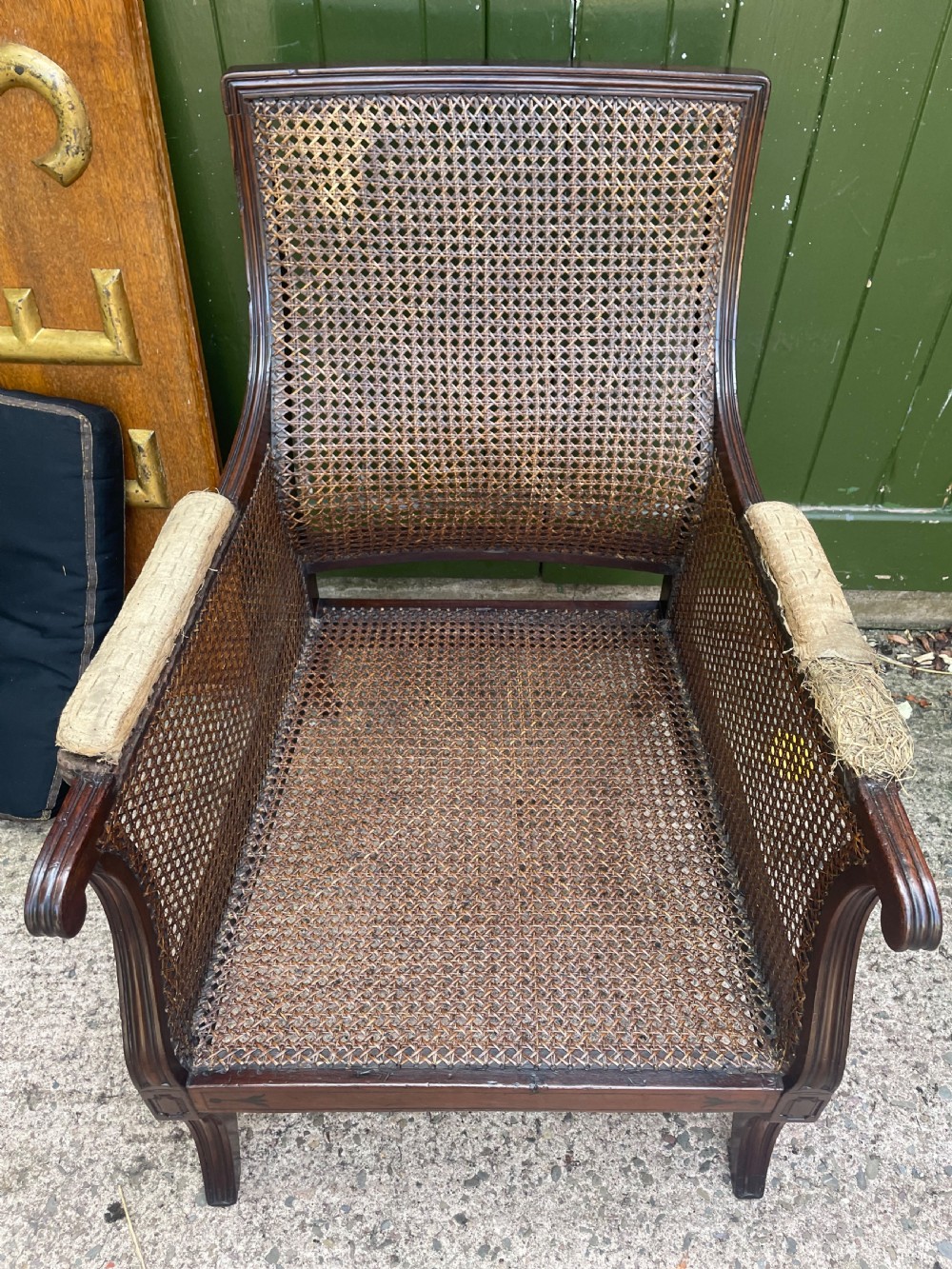 An early 19th-century Regency mahogany bergere armchair with woven cane back and sides, curved armrests, and a dark squab cushion. View XV