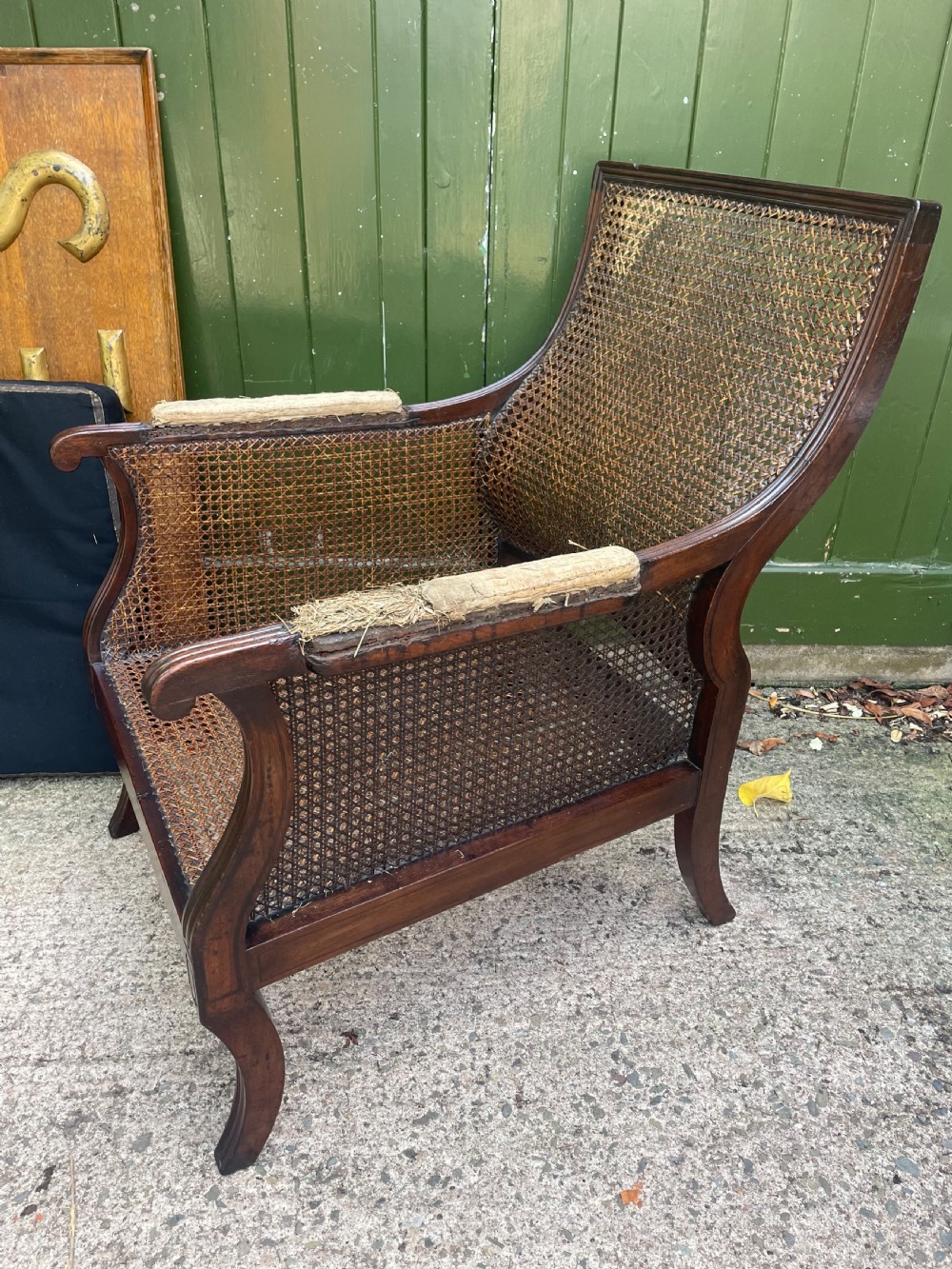 An early 19th-century Regency mahogany bergere armchair with woven cane back and sides, curved armrests, and a dark squab cushion. View XVII