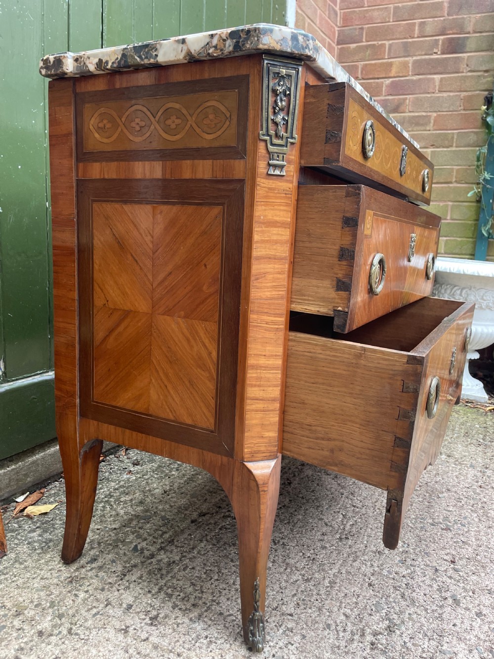 A late nineteenth-century French Louis XVI transitional style commode featuring marquetry wood veneers, brass ring handles, and a grey marble top. View IX