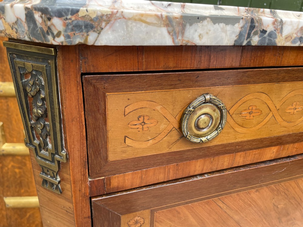 A late nineteenth-century French Louis XVI transitional style commode featuring marquetry wood veneers, brass ring handles, and a grey marble top. View XVI