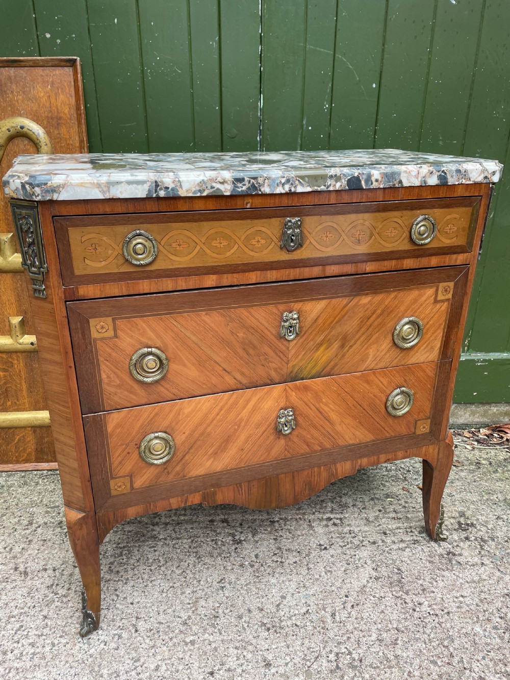 A late nineteenth-century French Louis XVI transitional style commode featuring marquetry wood veneers, brass ring handles, and a grey marble top. View XVIII