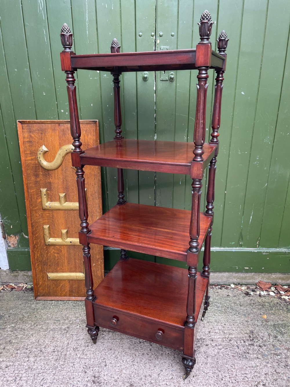 An early nineteenth-century George IV mahogany four-tier etagere featuring carved pinecone finials, turned supports, a single lower drawer, and brass castors.