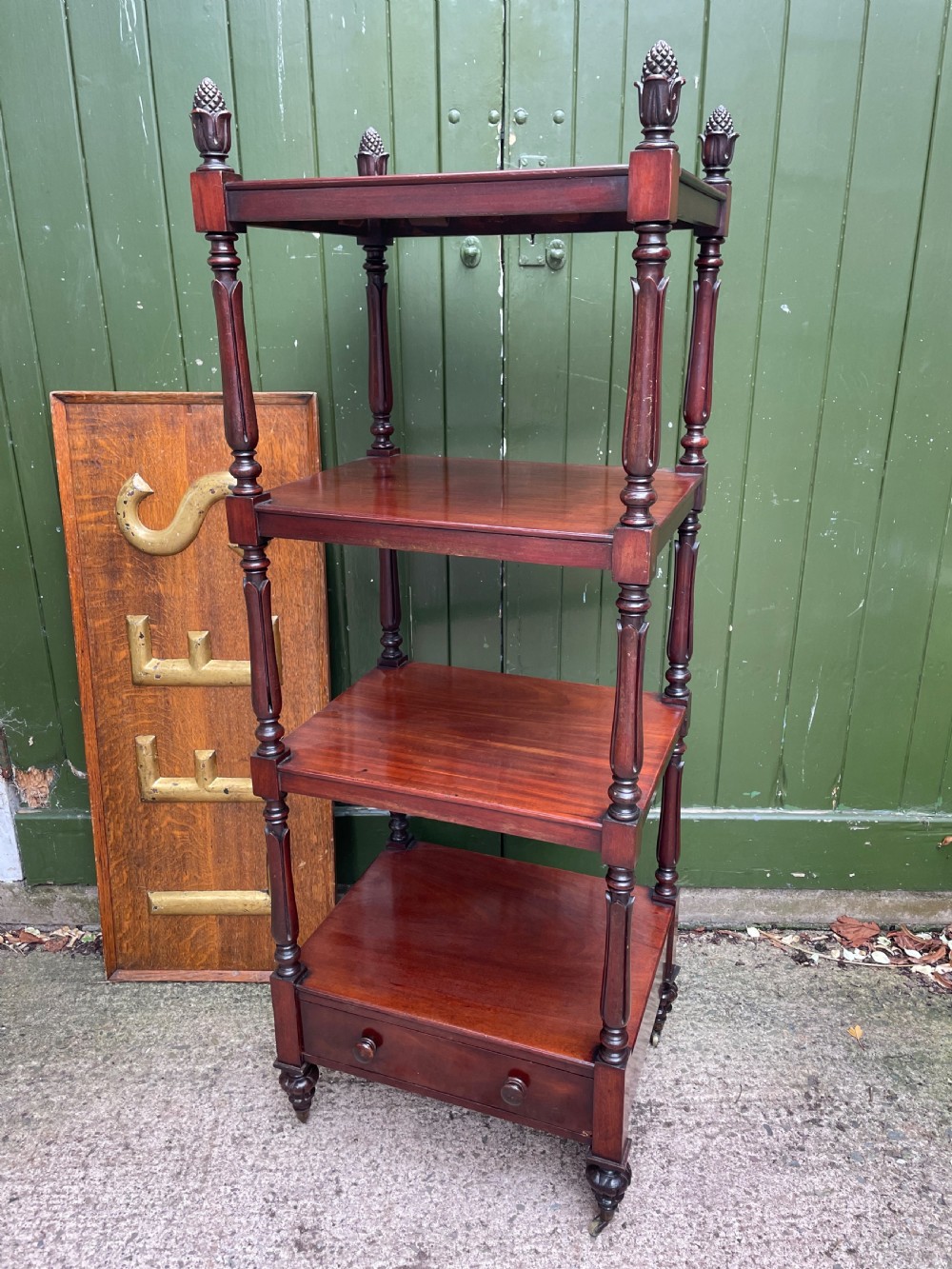 An early nineteenth-century George IV mahogany four-tier etagere featuring carved pinecone finials, turned supports, a single lower drawer, and brass castors. View II