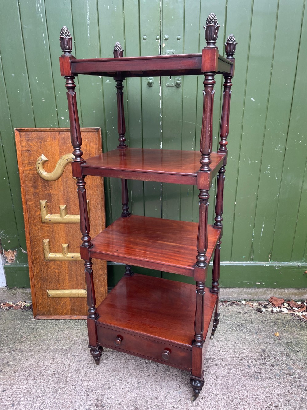 An early nineteenth-century George IV mahogany four-tier etagere featuring carved pinecone finials, turned supports, a single lower drawer, and brass castors. View VII