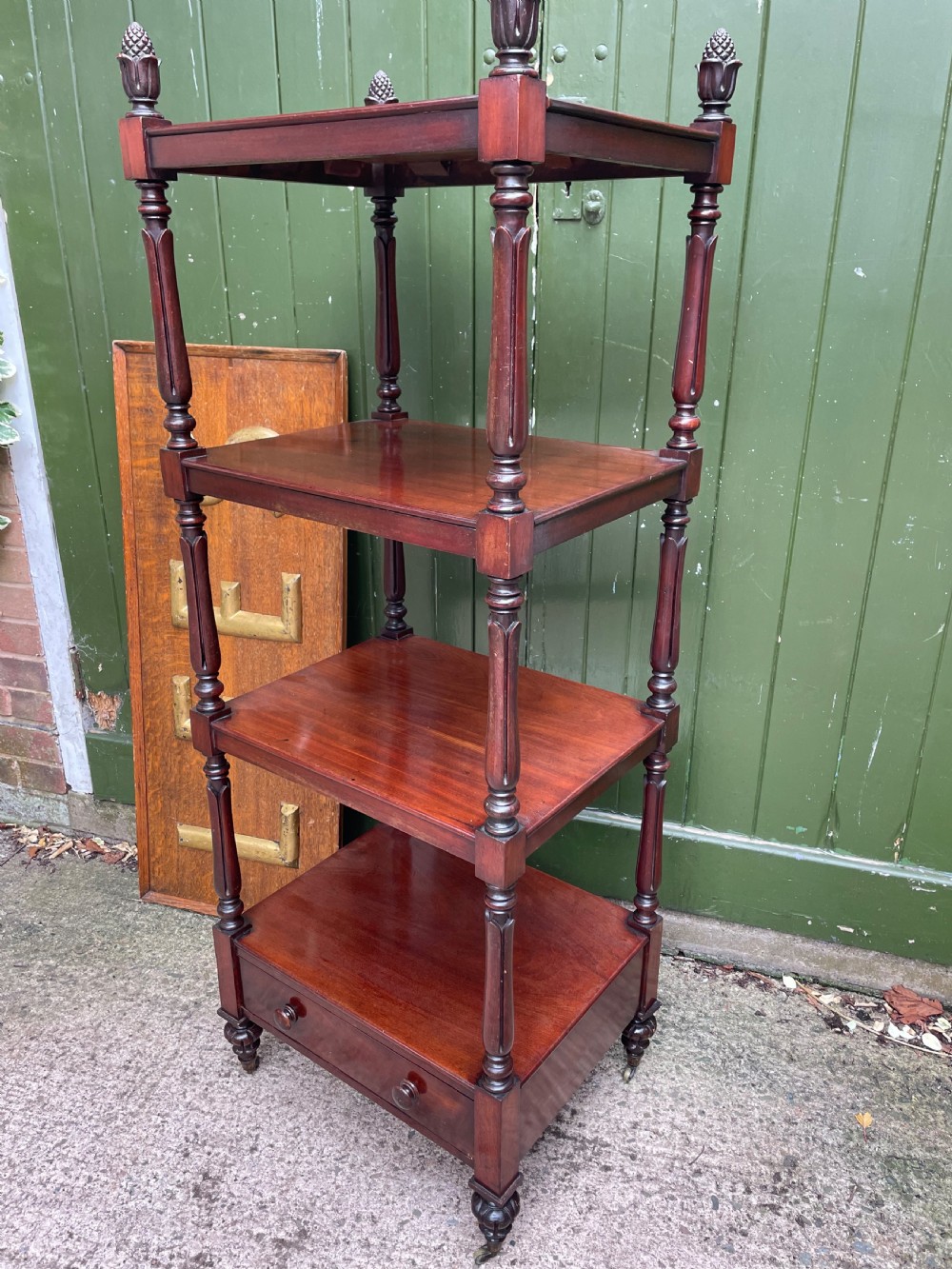 An early nineteenth-century George IV mahogany four-tier etagere featuring carved pinecone finials, turned supports, a single lower drawer, and brass castors. View VIII