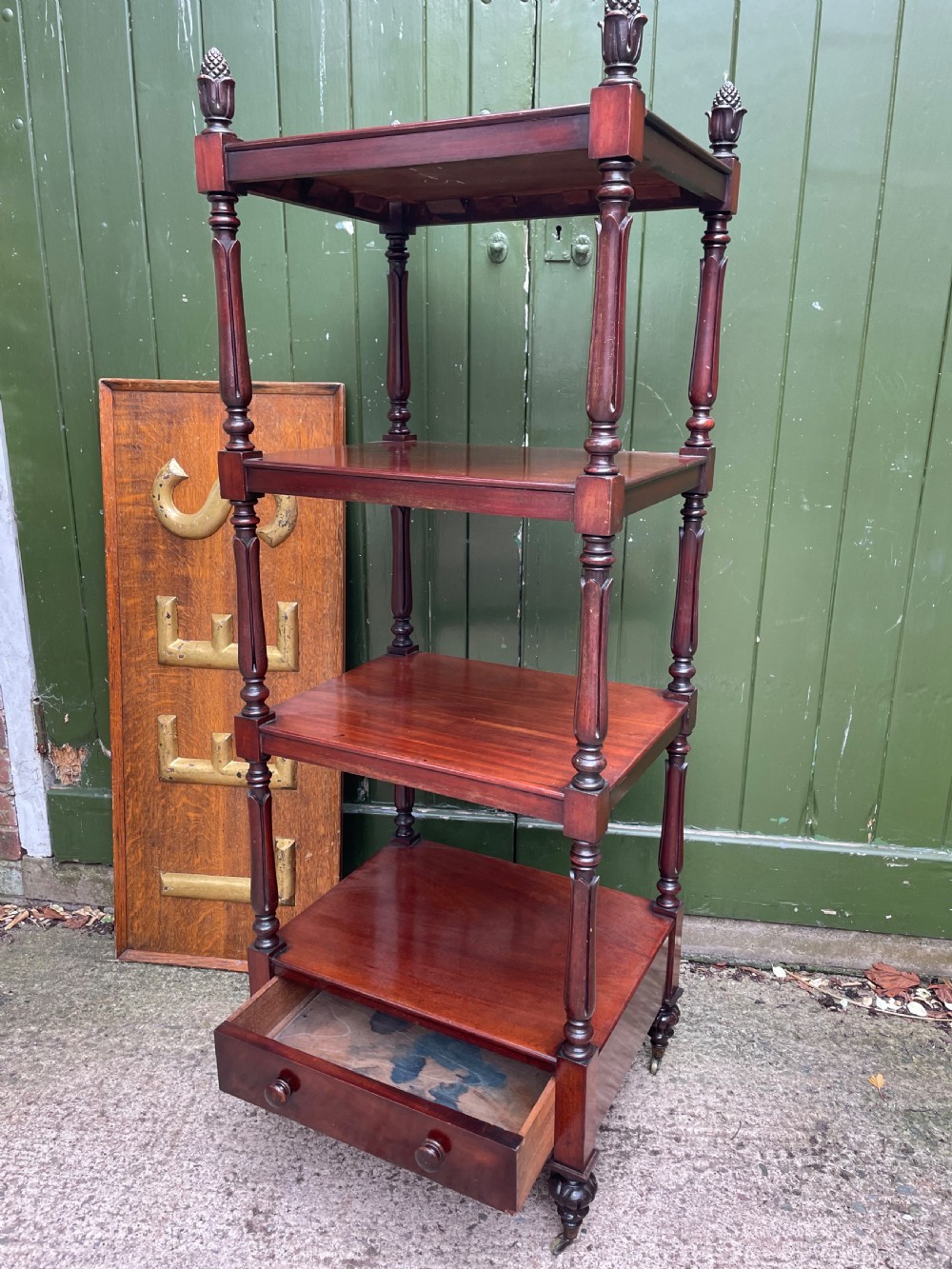 An early nineteenth-century George IV mahogany four-tier etagere featuring carved pinecone finials, turned supports, a single lower drawer, and brass castors. View IX