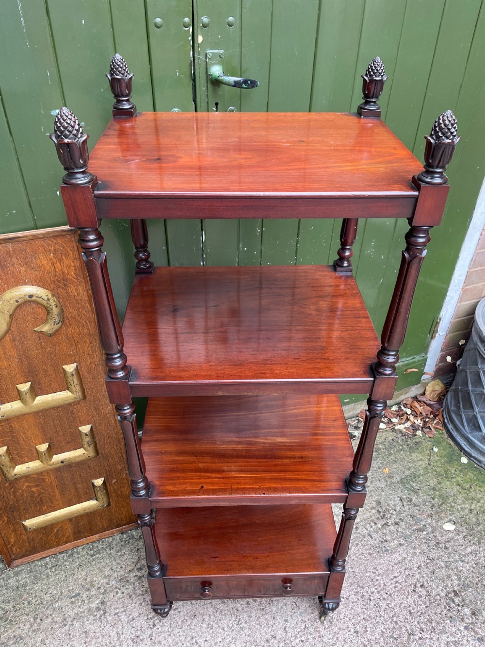An early nineteenth-century George IV mahogany four-tier etagere featuring carved pinecone finials, turned supports, a single lower drawer, and brass castors. View XII