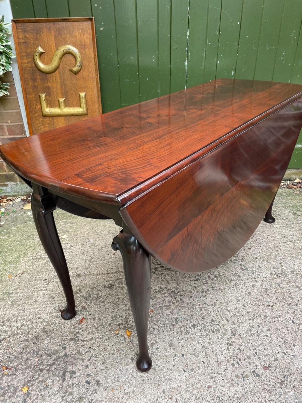 A mid-18th century George II Cuban mahogany drop-leaf table featuring an oval top, cabriole legs, and pad feet.
