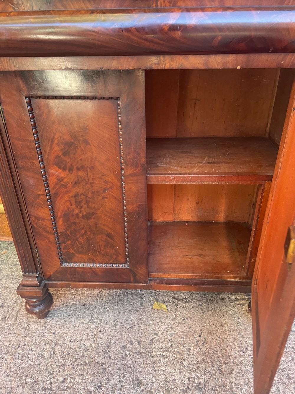 An early nineteenth-century George IV flame mahogany chiffonier featuring a raised shelf gallery with scroll supports above a two-door cabinet supported on turned bun feet. View VII