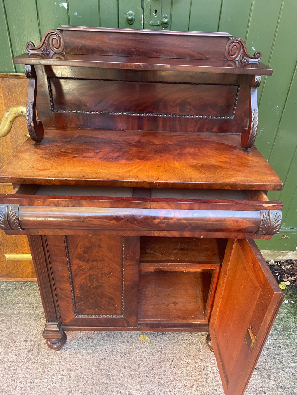 An early nineteenth-century George IV flame mahogany chiffonier featuring a raised shelf gallery with scroll supports above a two-door cabinet supported on turned bun feet. View VIII