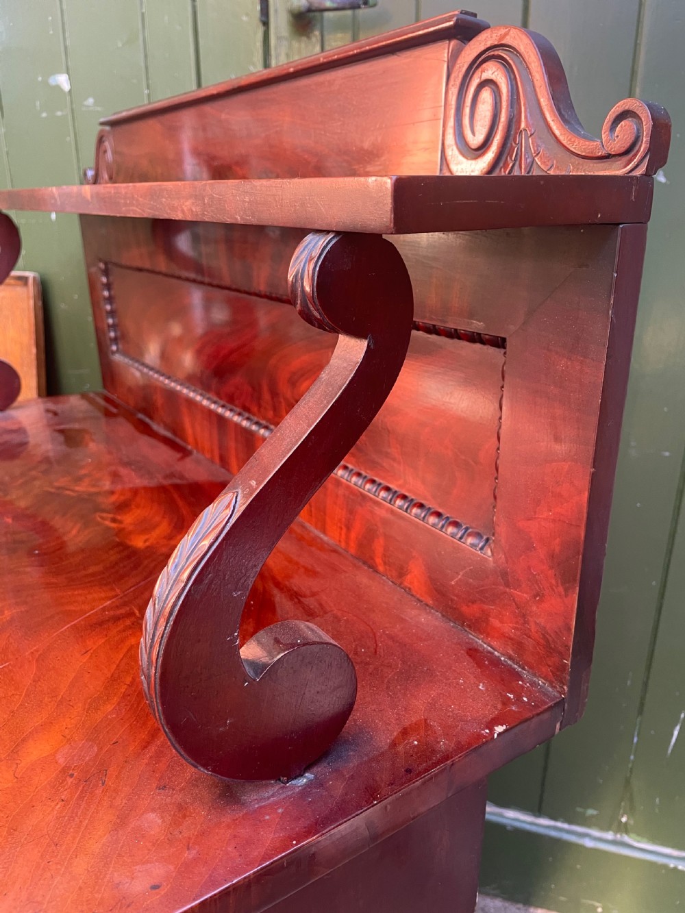 An early nineteenth-century George IV flame mahogany chiffonier featuring a raised shelf gallery with scroll supports above a two-door cabinet supported on turned bun feet. View XI