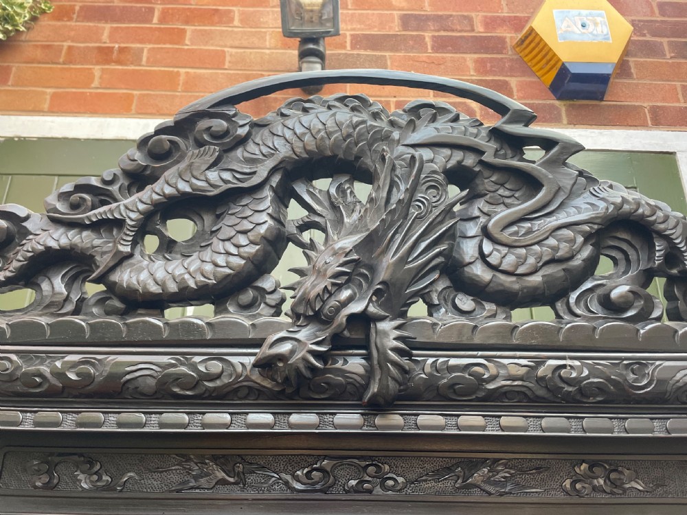An early 20th-century Japanese ebonised timber shodana display cabinet featuring detailed dragon and floral relief carvings, asymmetrical shelving, small cupboard doors, and a carved stand base. View III