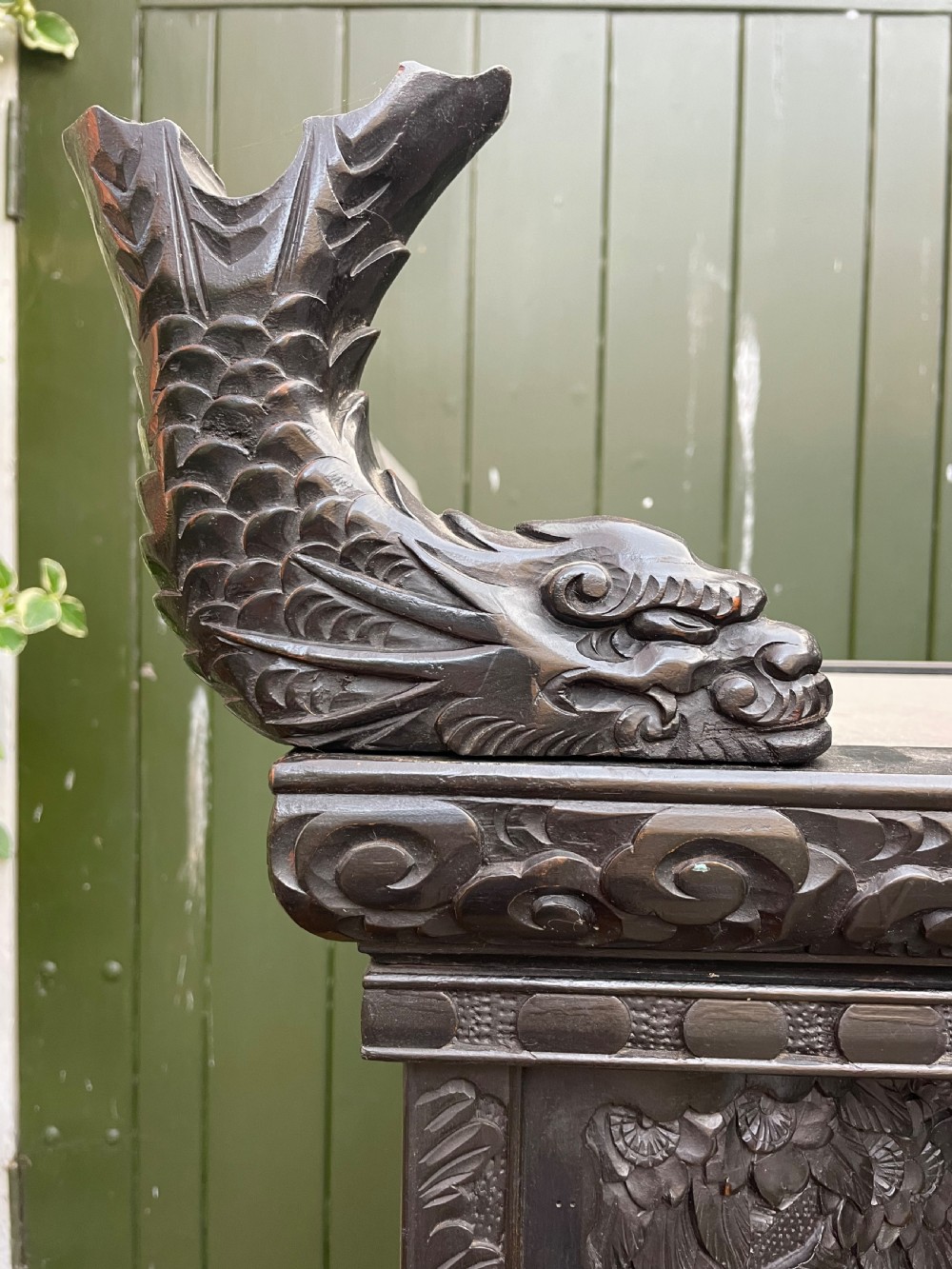 An early 20th-century Japanese ebonised timber shodana display cabinet featuring detailed dragon and floral relief carvings, asymmetrical shelving, small cupboard doors, and a carved stand base. View V
