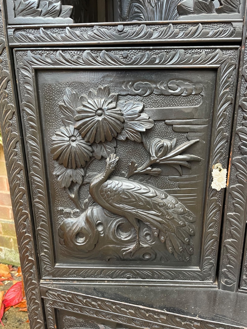 An early 20th-century Japanese ebonised timber shodana display cabinet featuring detailed dragon and floral relief carvings, asymmetrical shelving, small cupboard doors, and a carved stand base. View VII