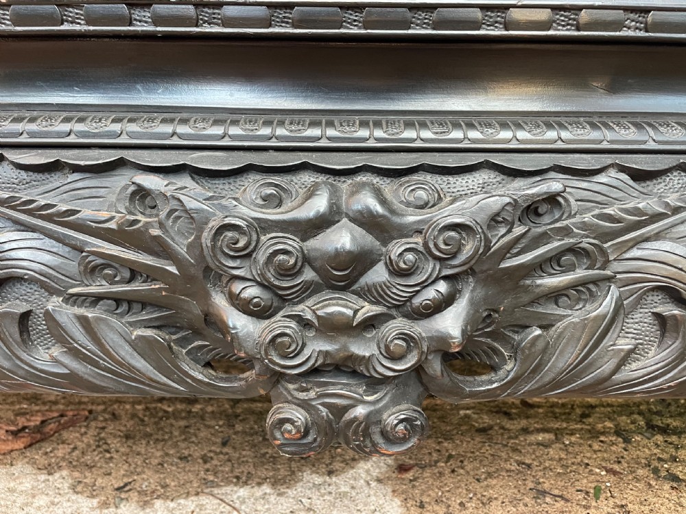 An early 20th-century Japanese ebonised timber shodana display cabinet featuring detailed dragon and floral relief carvings, asymmetrical shelving, small cupboard doors, and a carved stand base. View IX