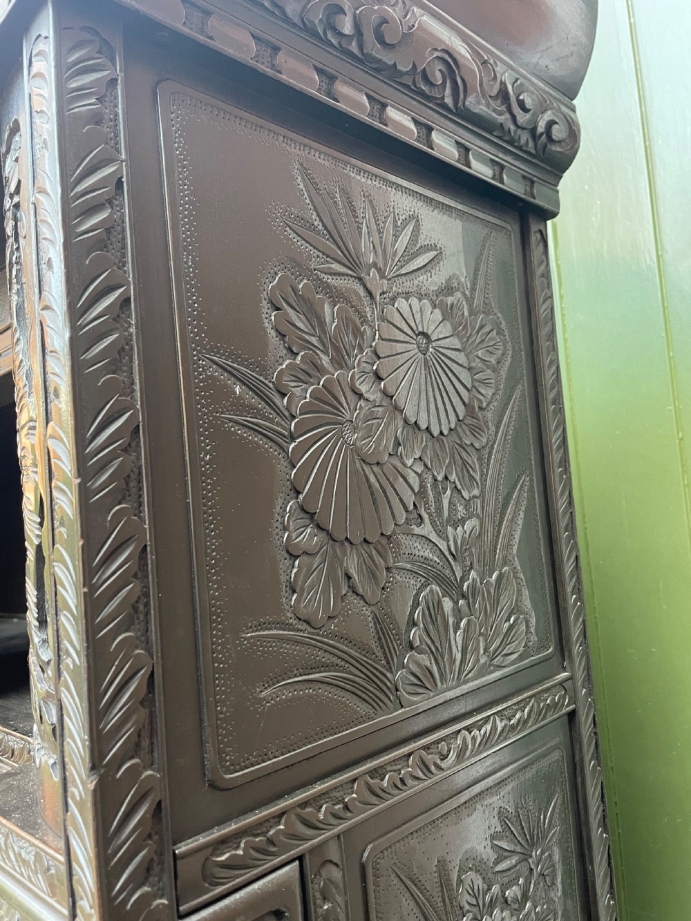 An early 20th-century Japanese ebonised timber shodana display cabinet featuring detailed dragon and floral relief carvings, asymmetrical shelving, small cupboard doors, and a carved stand base. View XIII