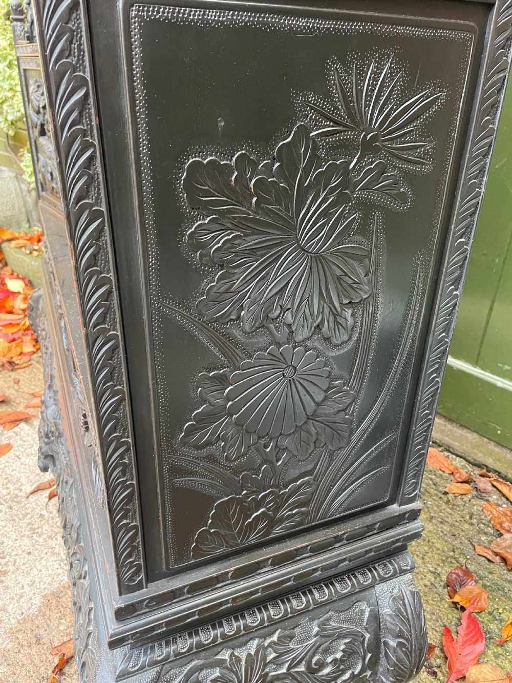 An early 20th-century Japanese ebonised timber shodana display cabinet featuring detailed dragon and floral relief carvings, asymmetrical shelving, small cupboard doors, and a carved stand base. View XVIII
