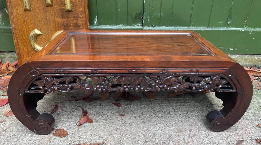 A low Chinese huali wood kang table featuring an openwork carved apron and scroll-end legs.
