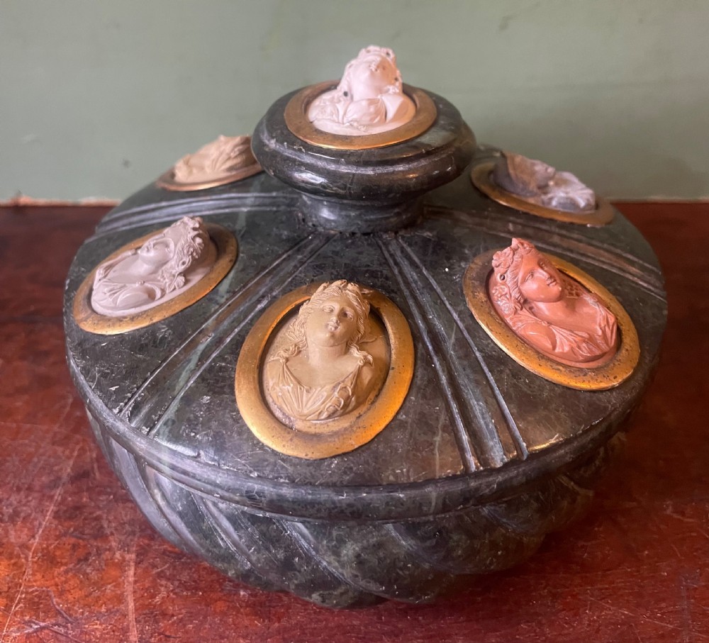 A circular dark green carved Prato Verde marble inkstand with fluted sides, set with six oval carved Vesuvian lava portrait cameos framed in brass mounts around a central raised finial.