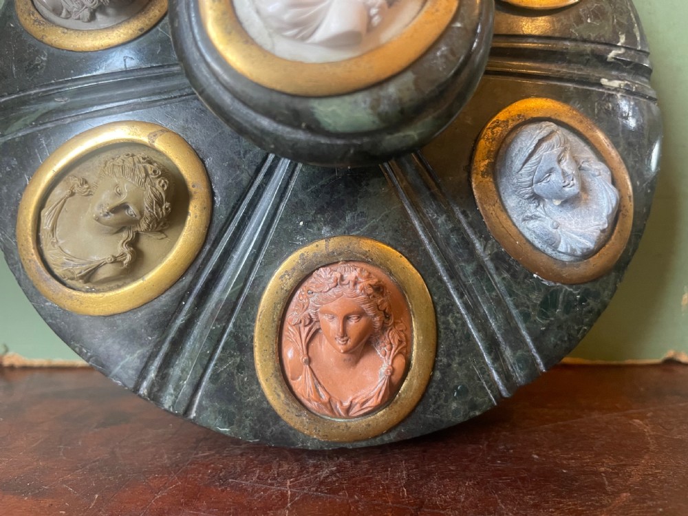 A circular dark green carved Prato Verde marble inkstand with fluted sides, set with six oval carved Vesuvian lava portrait cameos framed in brass mounts around a central raised finial. View VII