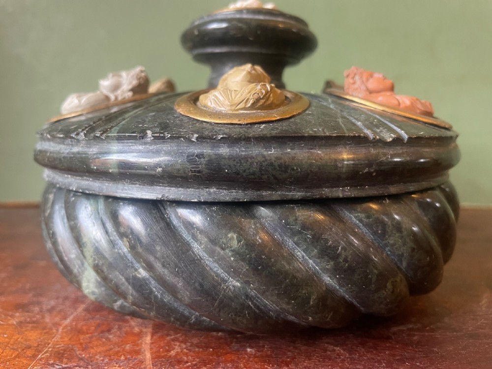 A circular dark green carved Prato Verde marble inkstand with fluted sides, set with six oval carved Vesuvian lava portrait cameos framed in brass mounts around a central raised finial. View XII