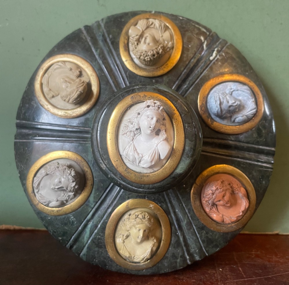 A circular dark green carved Prato Verde marble inkstand with fluted sides, set with six oval carved Vesuvian lava portrait cameos framed in brass mounts around a central raised finial. View XIII