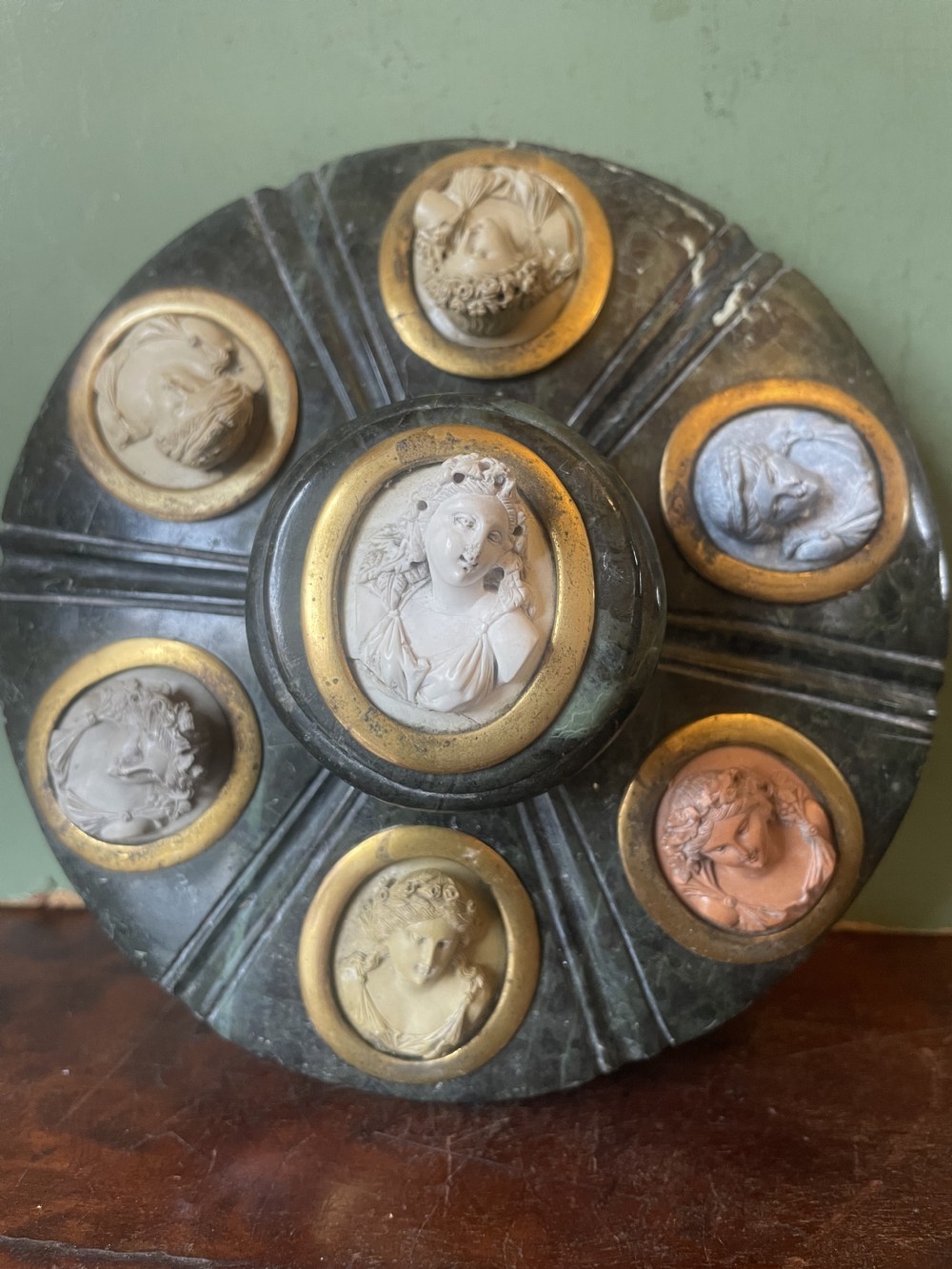 A circular dark green carved Prato Verde marble inkstand with fluted sides, set with six oval carved Vesuvian lava portrait cameos framed in brass mounts around a central raised finial. View XVI