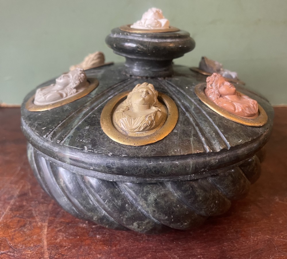 A circular dark green carved Prato Verde marble inkstand with fluted sides, set with six oval carved Vesuvian lava portrait cameos framed in brass mounts around a central raised finial. View XVIII