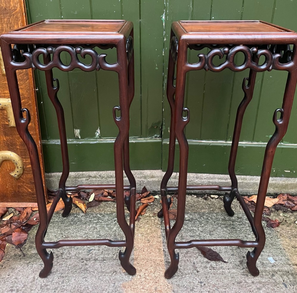 A pair of tall late 19th-century Chinese Qing Dynasty dark hardwood stands featuring square tops, openwork carved scroll aprons, and slender serpentine legs.