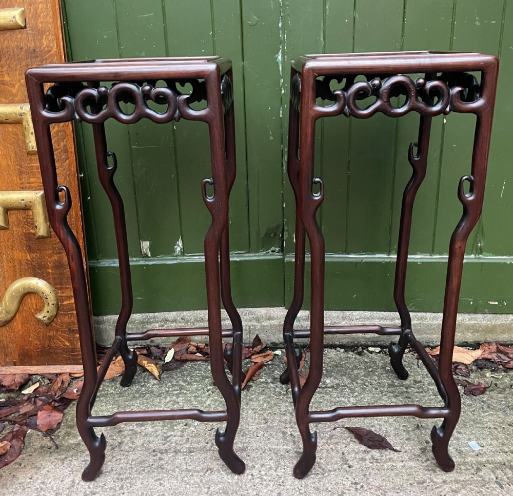 A pair of tall late 19th-century Chinese Qing Dynasty dark hardwood stands featuring square tops, openwork carved scroll aprons, and slender serpentine legs. View II