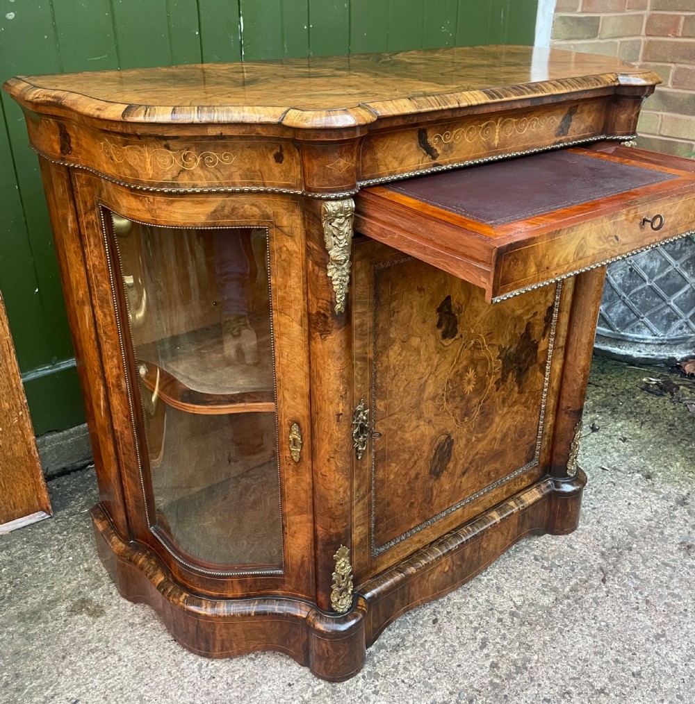 A mid-19th century Victorian burr walnut credenza featuring boxwood marquetry inlay, gilded ormolu mounts, a central drawer, and curved glass side display doors. View VII