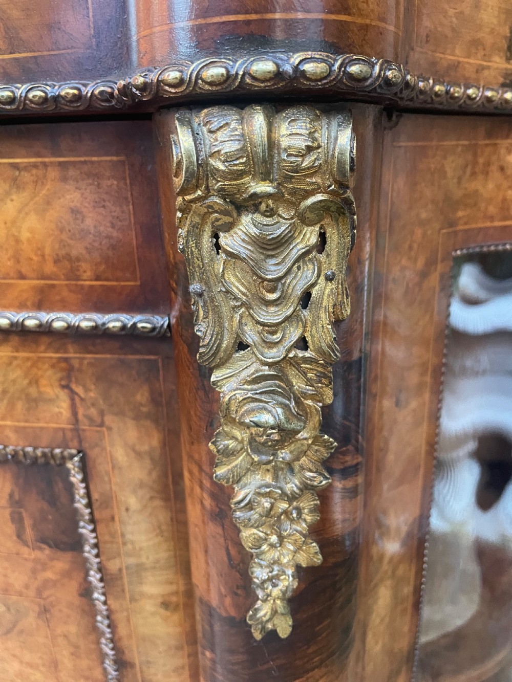 A mid-19th century Victorian burr walnut credenza featuring boxwood marquetry inlay, gilded ormolu mounts, a central drawer, and curved glass side display doors. View X