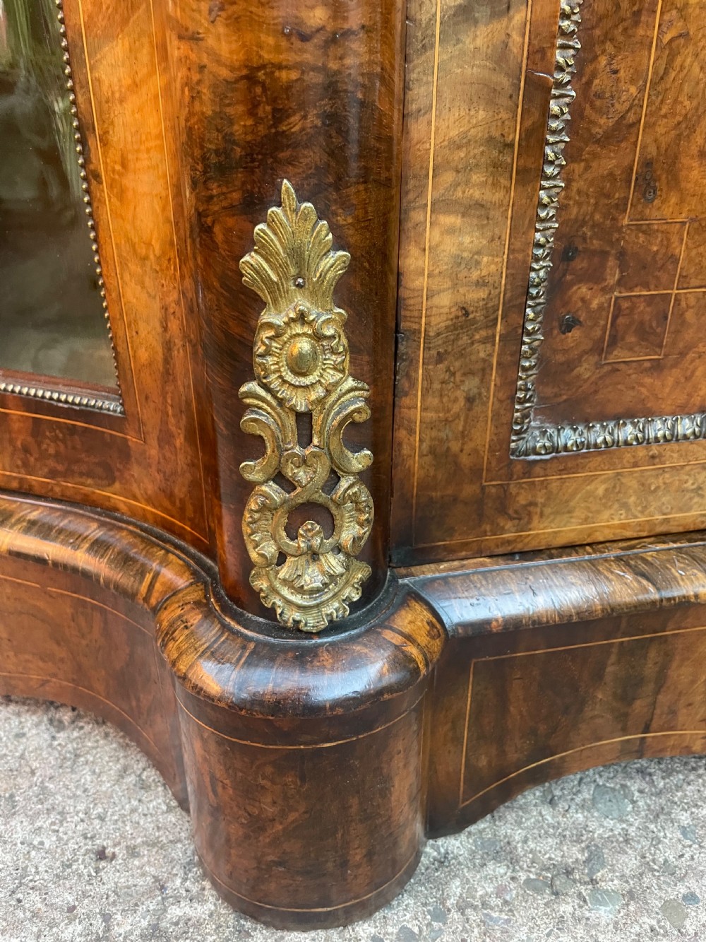 A mid-19th century Victorian burr walnut credenza featuring boxwood marquetry inlay, gilded ormolu mounts, a central drawer, and curved glass side display doors. View XI