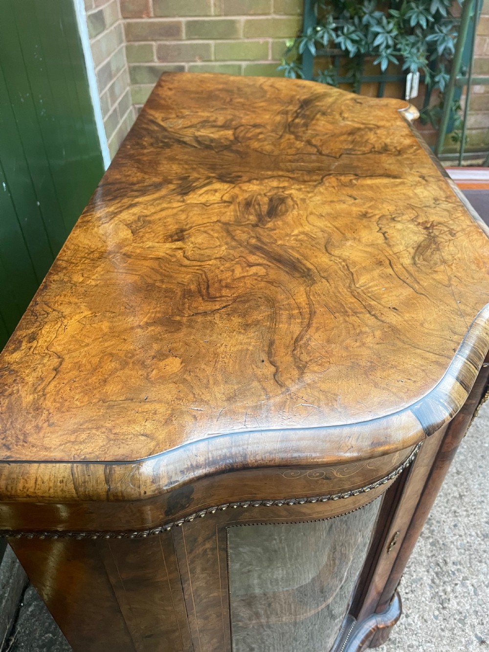 A mid-19th century Victorian burr walnut credenza featuring boxwood marquetry inlay, gilded ormolu mounts, a central drawer, and curved glass side display doors. View XIII