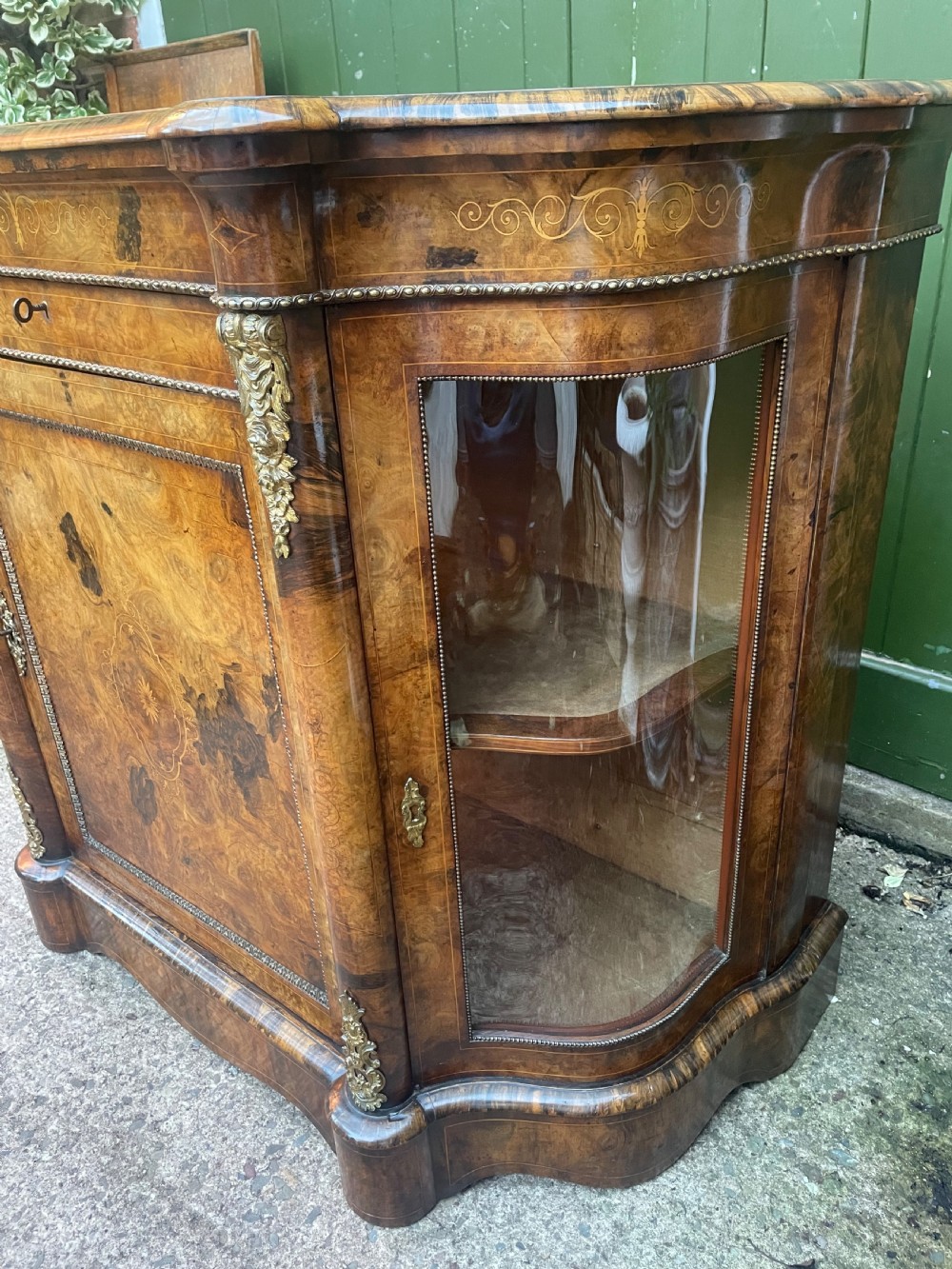 A mid-19th century Victorian burr walnut credenza featuring boxwood marquetry inlay, gilded ormolu mounts, a central drawer, and curved glass side display doors. View XV