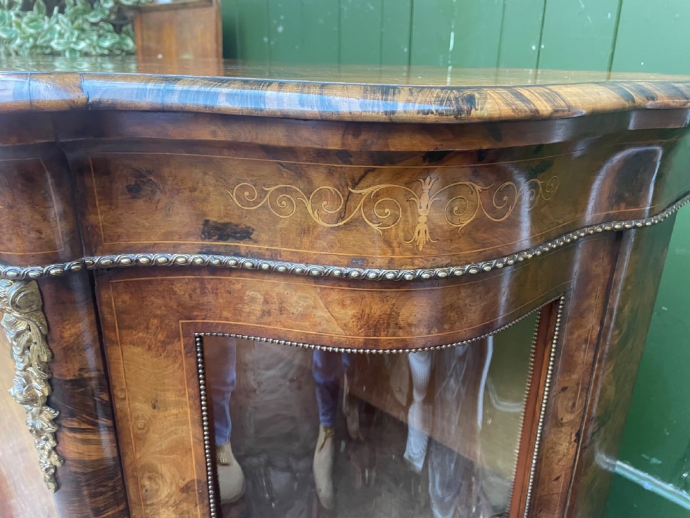 A mid-19th century Victorian burr walnut credenza featuring boxwood marquetry inlay, gilded ormolu mounts, a central drawer, and curved glass side display doors. View XVI