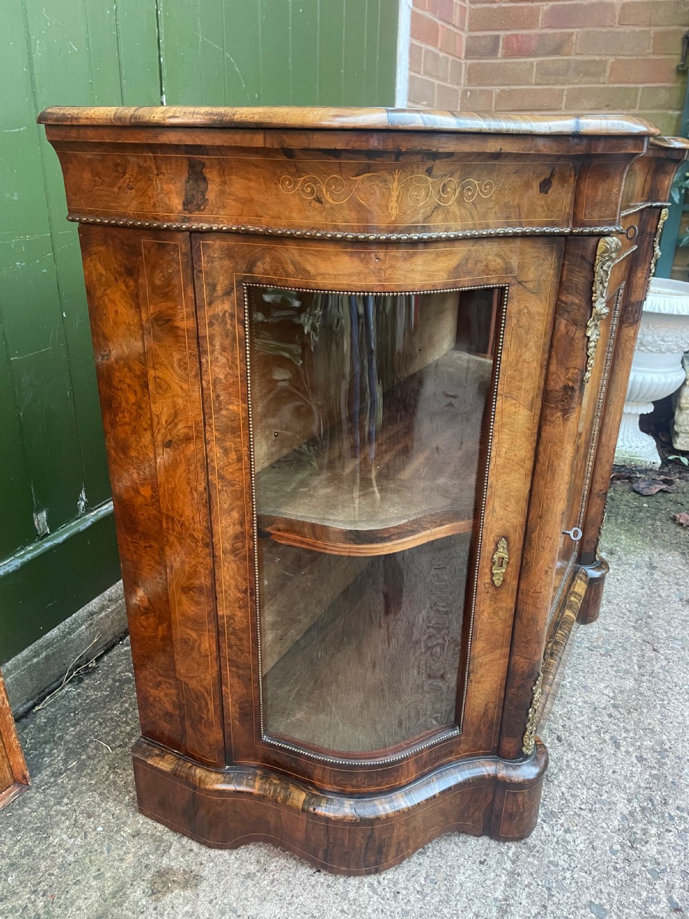 A mid-19th century Victorian burr walnut credenza featuring boxwood marquetry inlay, gilded ormolu mounts, a central drawer, and curved glass side display doors. View XVII