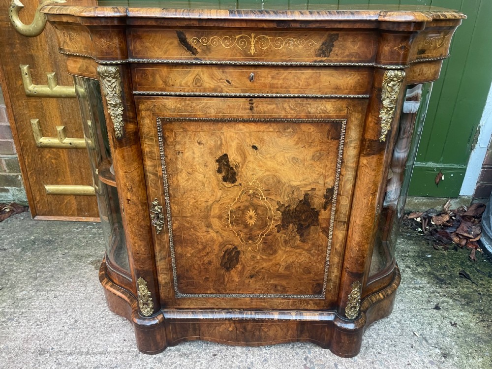 A mid-19th century Victorian burr walnut credenza featuring boxwood marquetry inlay, gilded ormolu mounts, a central drawer, and curved glass side display doors. View XVIII