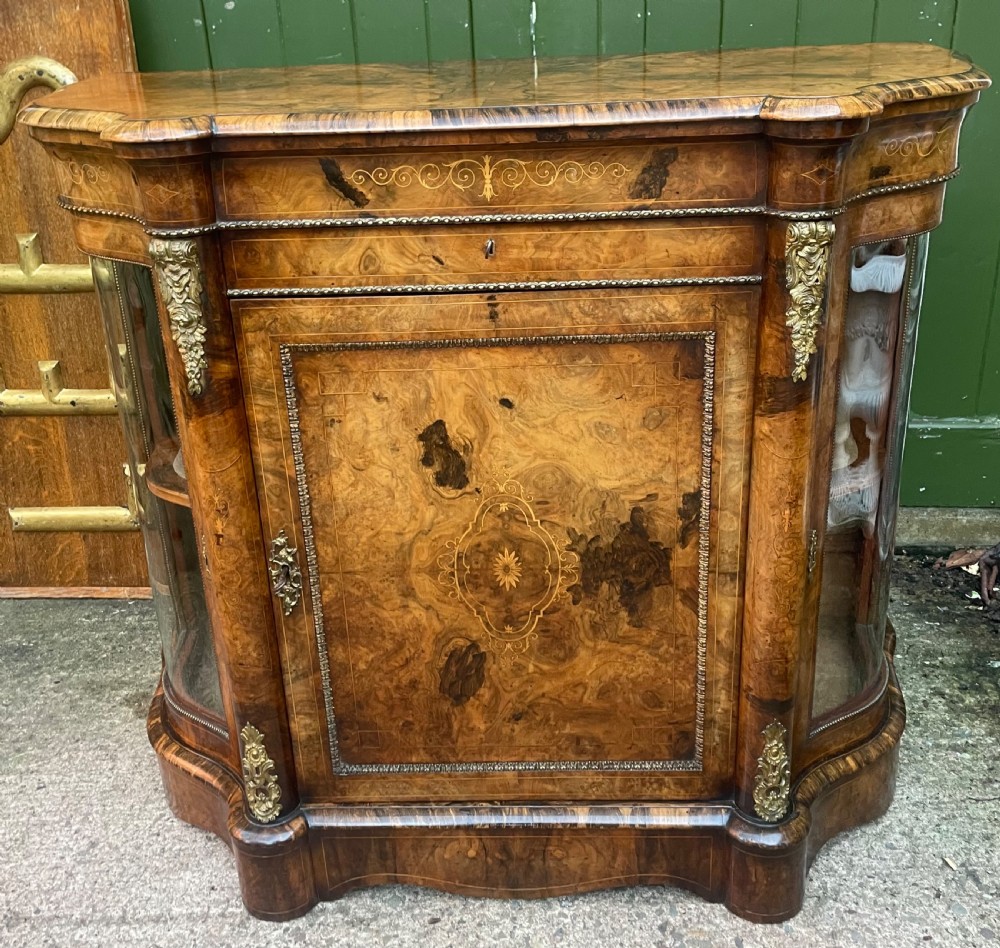 A mid-19th century Victorian burr walnut credenza featuring boxwood marquetry inlay, gilded ormolu mounts, a central drawer, and curved glass side display doors. View XIX