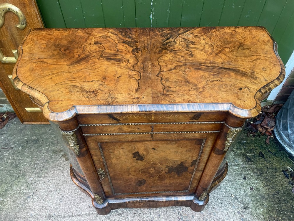 A mid-19th century Victorian burr walnut credenza featuring boxwood marquetry inlay, gilded ormolu mounts, a central drawer, and curved glass side display doors. View XX